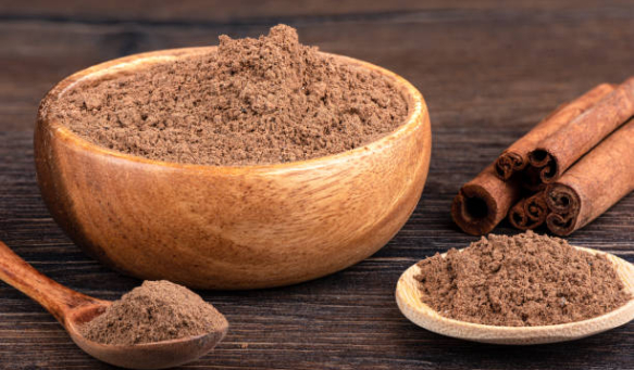 Cinnamon sticks and ground cinnamon in a bowl, on a spoon over a wooden background. Close up.